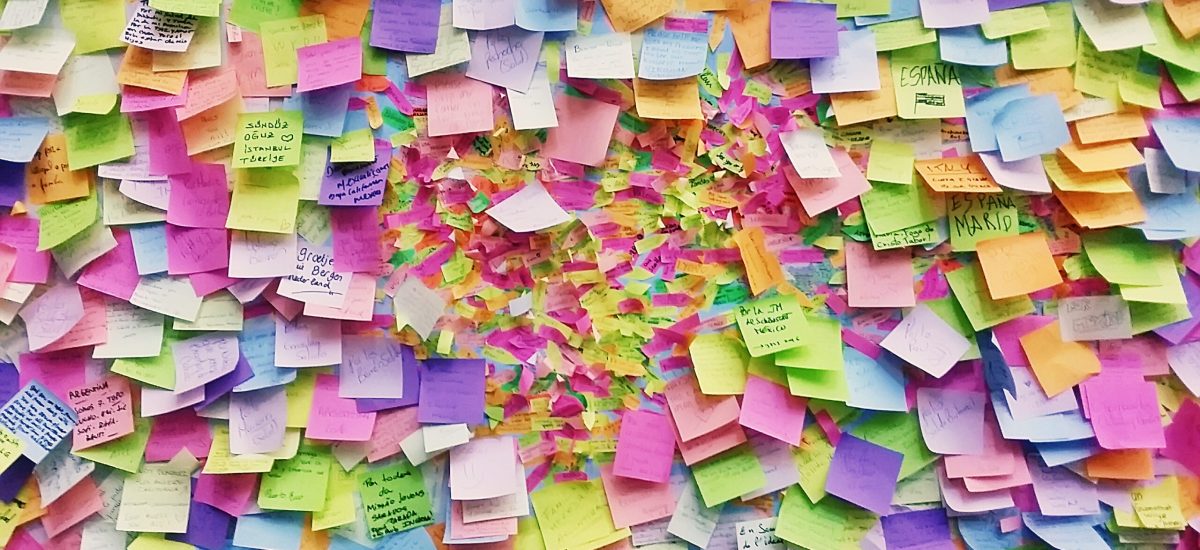 Wall full of multi colored adhesive papers with positive messages on it, this wall is inside Our Lady of Victory Church in Prague.